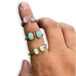Three silver rings with rectangular  cabochon stones shown worn on a person's fingers against a white background.