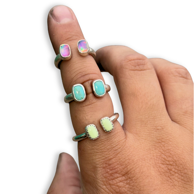 Three silver rings with rectangular  cabochon stones shown worn on a person's fingers against a white background.